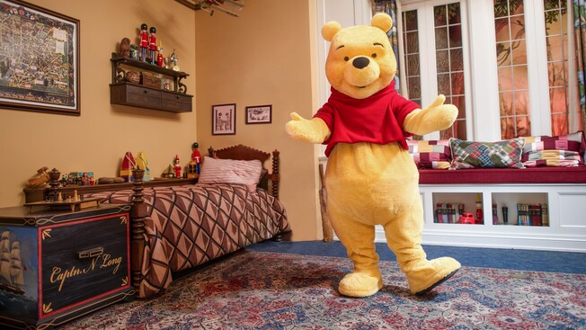 Winnie the Pooh parado en medio de un dormitorio con muchos juguetes, libros y cojines