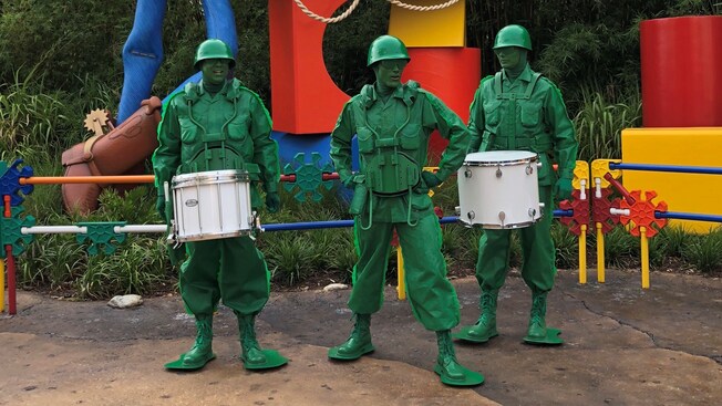 The Green Army Man Drum Corps stand, ready to play, in front of Woody and the Toy Story Land sign