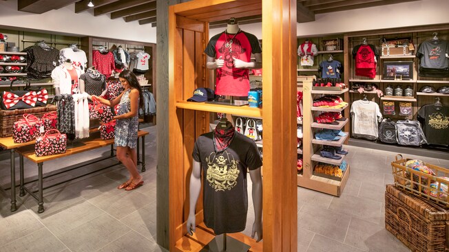 O interior da Calypso Trading Post com uma grande variedade de produtos em exposição e uma compradora analisando uma bolsa temática da Minnie