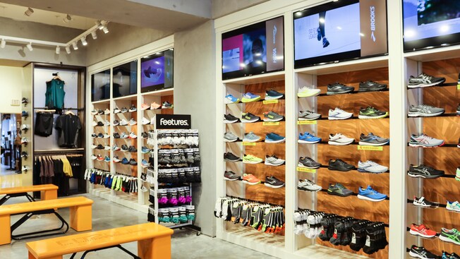 Interior of Fit2Run featuring sneaker wall displays, racks of running accessories, sitting benches and TV monitors