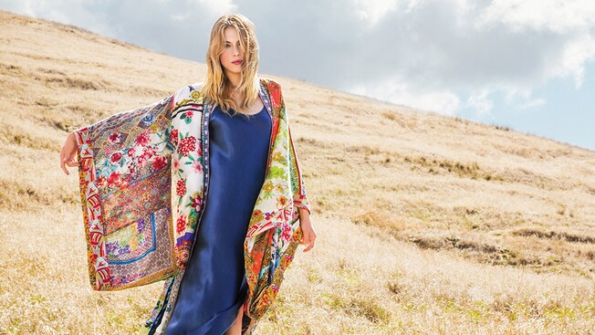 A woman in a meadow models a silk dress and patterned kimono wrap from the Johnny Was boutique