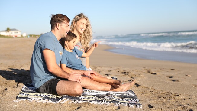 A family sits on a beach and smiles at the waves