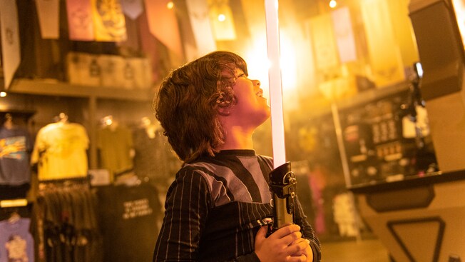 Amidst store displays, a young boy holds a glowing lightsaber 