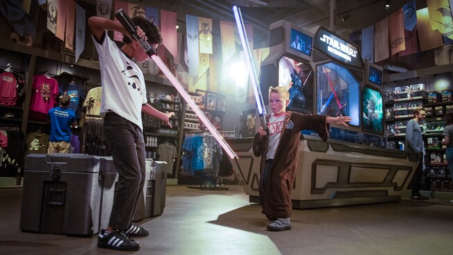 Amidst store displays, 2 young boys pretend to battle with lightsabers