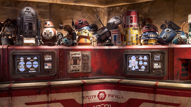 Two illuminated monitors below a crowded shelf featuring a multitude of spare astromech droid parts inside Droid Depot