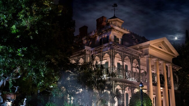 The formidable exterior of the Haunted Mansion is illuminated under moonlit skies