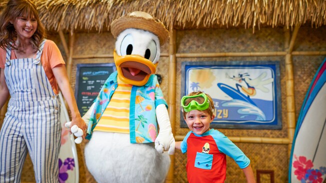 Donald Duck camina de la mano con una mujer y su hijo frente a un restaurante estilo cabaña