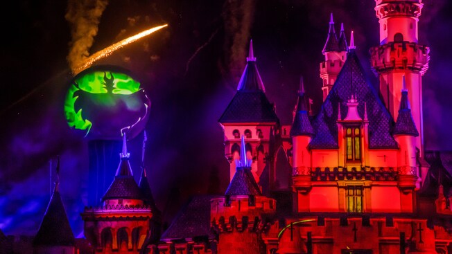 Sparkles fly in the night by a large projected image of Maleficent, next to Sleeping Beauty Castle during Halloween Time at the Disneyland Resort