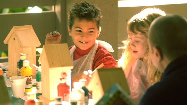 A boy and girl at a crafts table painting birdhouses