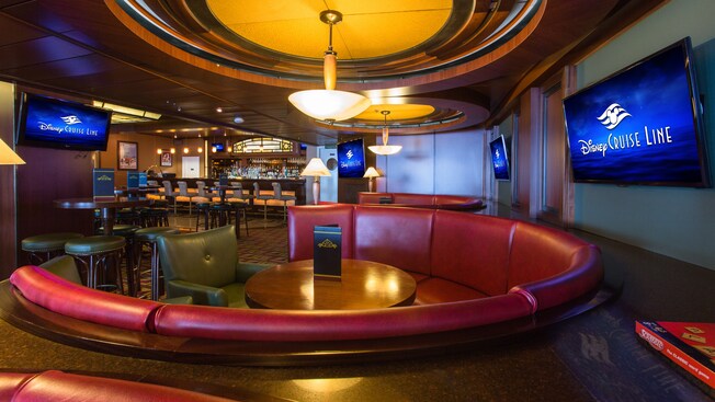 A large, circular couch with shiny upholstery surrounds a table at a sports bar
