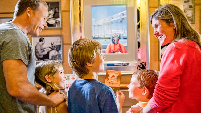 A young boy, with his family, holds a game card, by enchanted art, to play the Muppet Adventure Game A young boy, with his family, holds a game card, by enchanted art, to play the Muppet Adventure Game