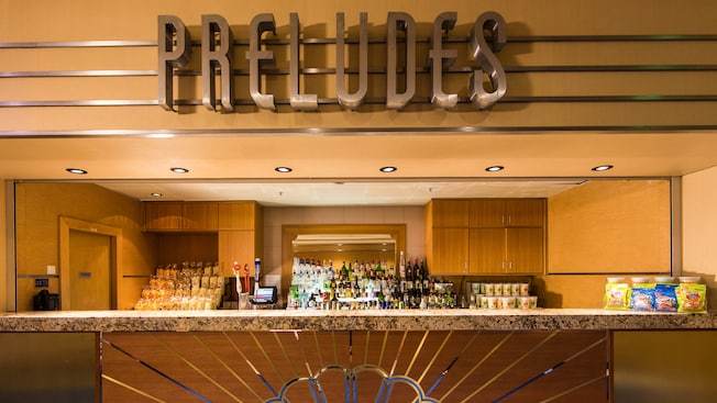 A sign says Preludes over a quick service restaurant bar with snacks on the counter and beverages behind it A sign says Preludes over a quick service restaurant bar with snacks on the counter and beverages behind it