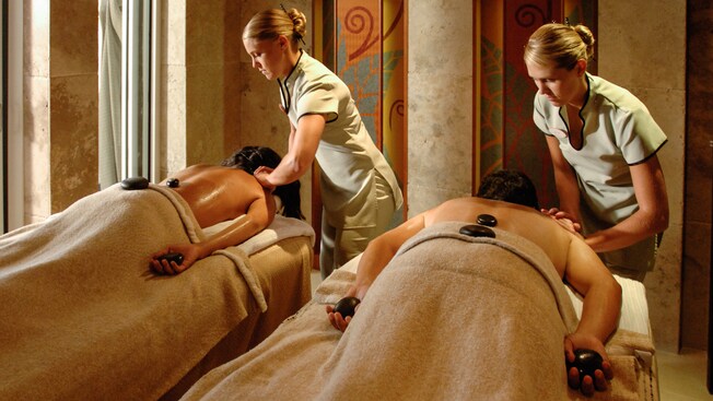 A couple lay face down on treatment tables while each receives a massage from a therapist
