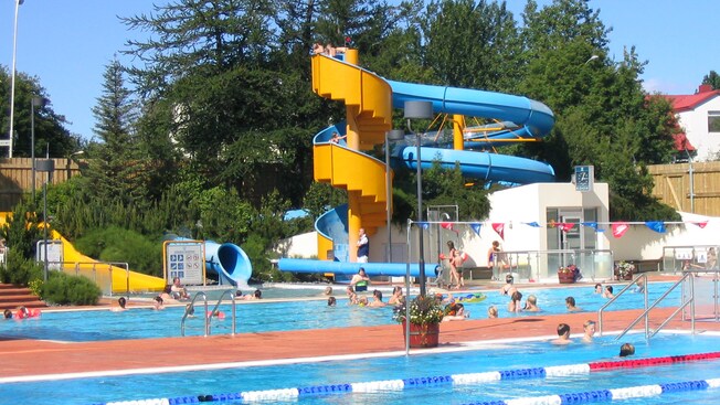Familias y niños disfrutando de una piscina comunitaria con un tobogán de agua en espiral
