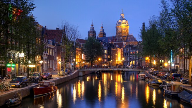 An Amsterdam canal at dusk is lined with small boats and historic architecture