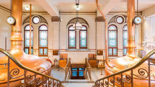 The 19th century interior of the Heineken Museum reveals 2 large stills, stained glass windows, brick walls and a staircase with decorative brass handrails
