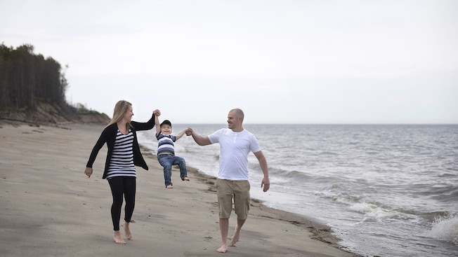 A couple swings their young son up in the air between them as they walk along the beach A couple swings their young son up in the air between them as they walk along the beach