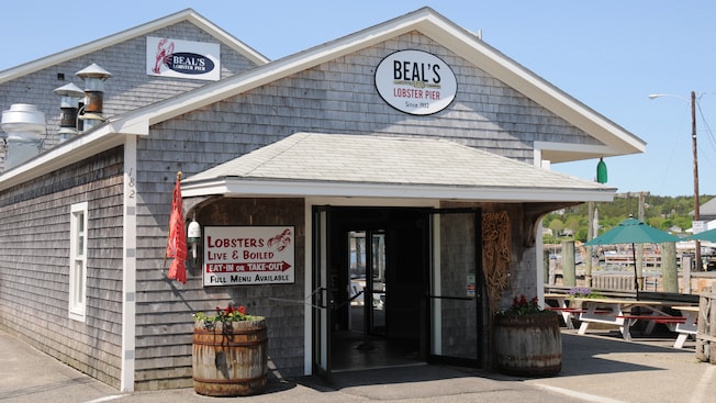 Building exterior with signs that say BEALS, LOBSTER PIER, Since 1932 and LOBSTERS, LIVE AND BOILED, EAT IN OR TAKE OUT, FULL MENU AVAILABLE Building exterior with signs that say BEALS, LOBSTER PIER, Since 1932 and LOBSTERS, LIVE AND BOILED, EAT IN OR TAKE OUT, FULL MENU AVAILABLE