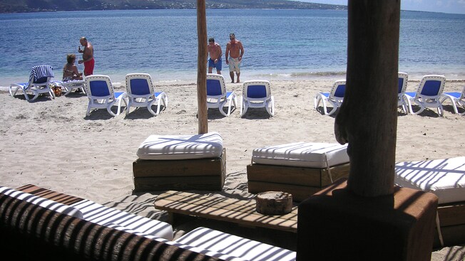 Guests relaxing on a sandy shoreline with beach chairs and a shaded seating area