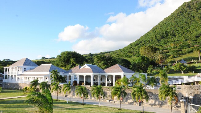 Palm trees and mountainous vegetation surround the colonial exterior of the Fairview Great House and Botanical Garden in Saint Kitts, West Indies