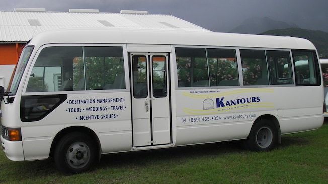 A passenger touring van by Kantours Tours rests on a grass field