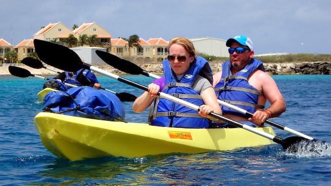 2 couples in kayaks near a beach with buildings 2 couples in kayaks near a beach with buildings