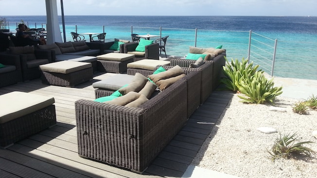 A seating area with couches, chairs, pillows and tables on a beach A seating area with couches, chairs, pillows and tables on a beach