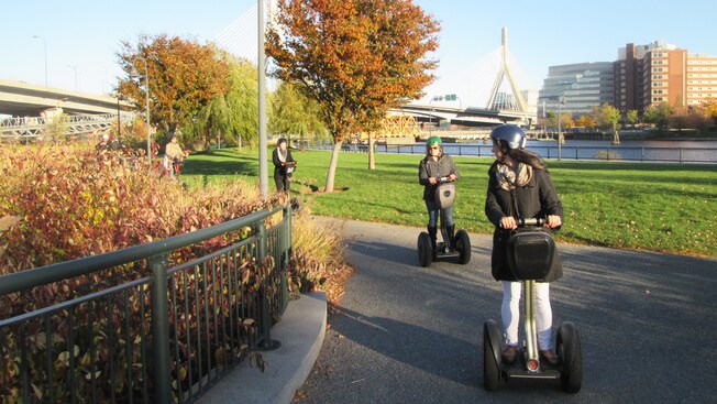 People wearing helmets and riding Segways around a bend