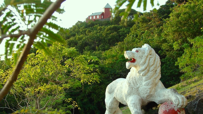 A carved statue of a lion is surrounded by lush trees and a house on a hill A carved statue of a lion is surrounded by lush trees and a house on a hill