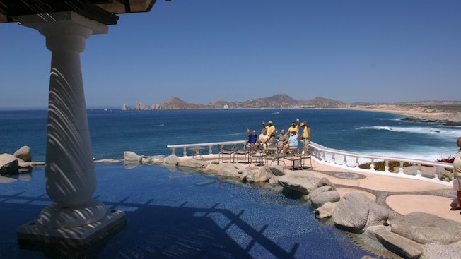 A group of adults sitting by a fountain wave at the camera with the ocean behind them A group of adults sitting by a fountain wave at the camera with the ocean behind them