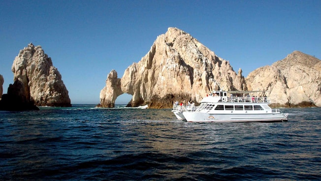 Um catamarã repleto de passageiros fazendo um cruzeiro ao lado da formação rochosa de El Arco rock em Cabo San Lucas Um catamarã repleto de passageiros fazendo um cruzeiro ao lado da formação rochosa de El Arco rock em Cabo San Lucas