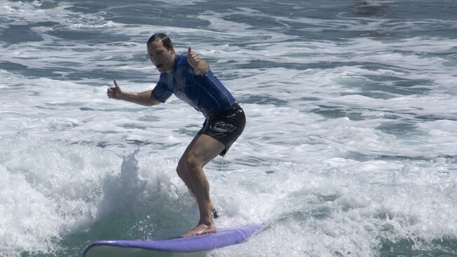 Man riding a surfboard on a foamy ocean wave with two thumbs up