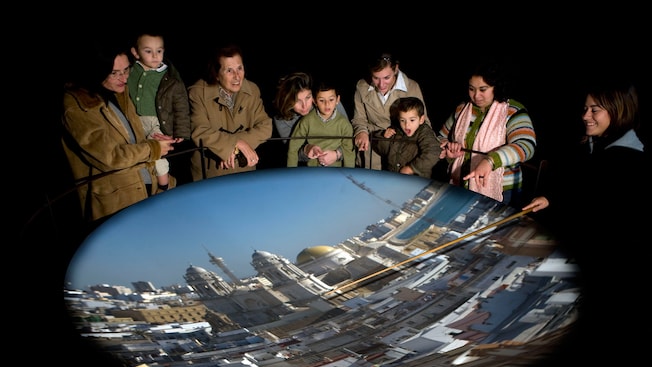 Adults and children around a camera obscura as a guide points out city buildings in its projected image Adults and children around a camera obscura as a guide points out city buildings in its projected image