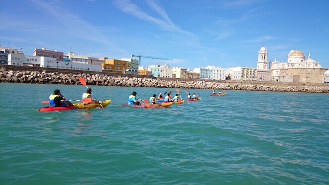 Six pairs of Guests paddle kayaks in water near a stone wall
