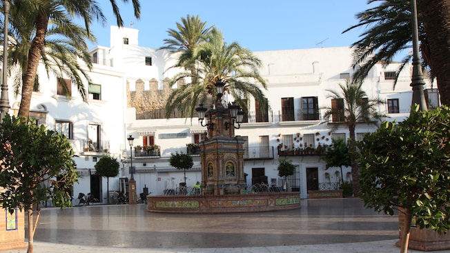 A fountain at the center of a Spanish apartment building courtyard has porcelain tile and palm trees A fountain at the center of a Spanish apartment building courtyard has porcelain tile and palm trees