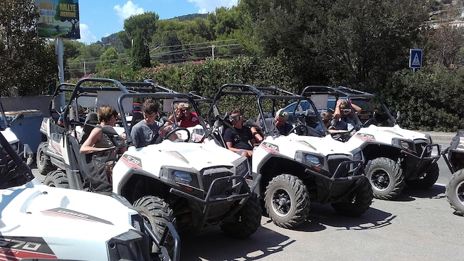 Un grupo de personas sentadas en buggies para 2 personas en un área de estacionamiento con un fondo de árboles cerca de un letrero que dice Buggy VTT Rallye Adventure Un grupo de personas sentadas en buggies para 2 personas en un área de estacionamiento con un fondo de árboles cerca de un letrero que dice Buggy VTT Rallye Adventure