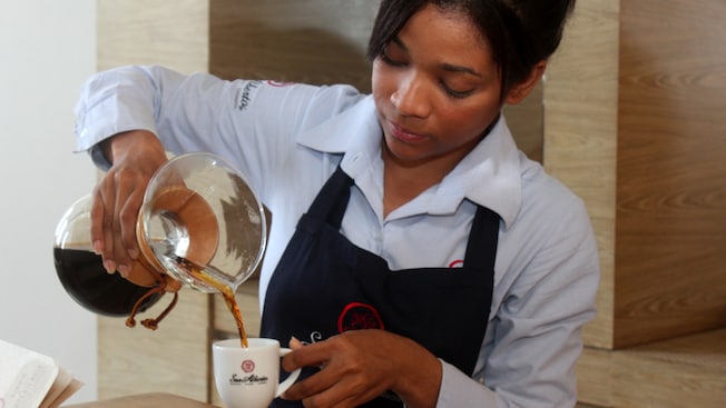 Un mesero uniformado sirve café de una garrafa a una taza