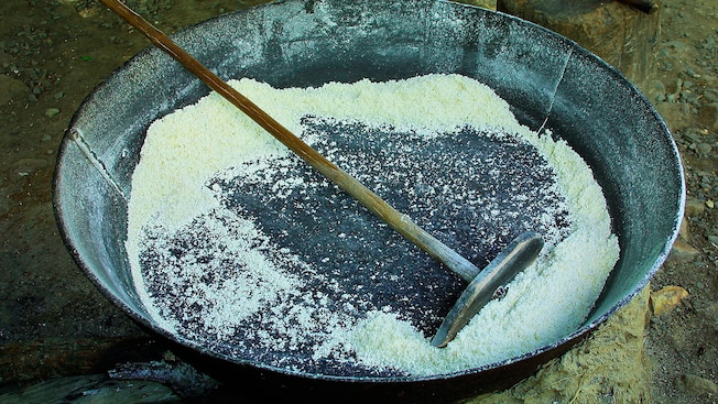 A long, wooden cooking tool with a flat end parts flour in a metal basin A long, wooden cooking tool with a flat end parts flour in a metal basin