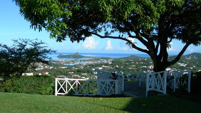 Um pátio com uma cerca de madeira tem vista para a distante lâmina d’água da sombra de uma grande árvore