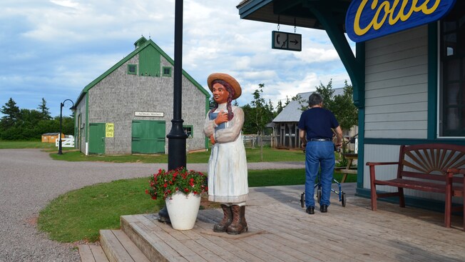 A figure of the Anne of Green Gables outside a cluster of 19th century farmhouse buildings