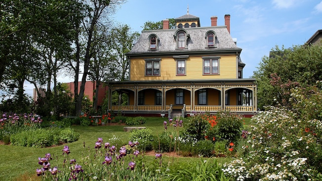 Un edificio de varios pisos con un pórtico envolvente, ventanas, chimeneas y un patio bien cuidado con flores y más Un edificio de varios pisos con un pórtico envolvente, ventanas, chimeneas y un patio bien cuidado con flores y más