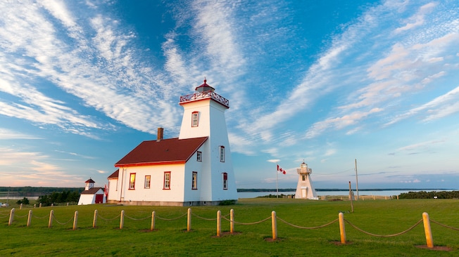A lighthouse by the water next to a flagpole featuring the Canadian flag A lighthouse by the water next to a flagpole featuring the Canadian flag