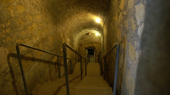 An arched, brick stairwell leading down to a door with a light over it