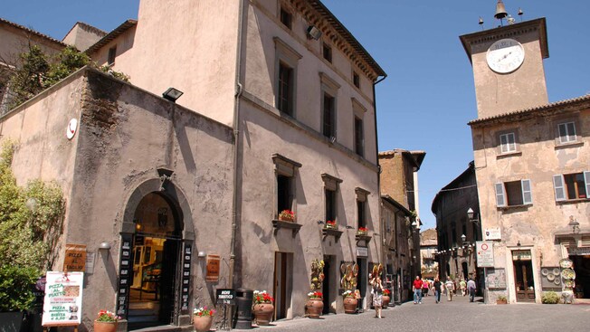People walk by shops and restaurants on an Italian street corner