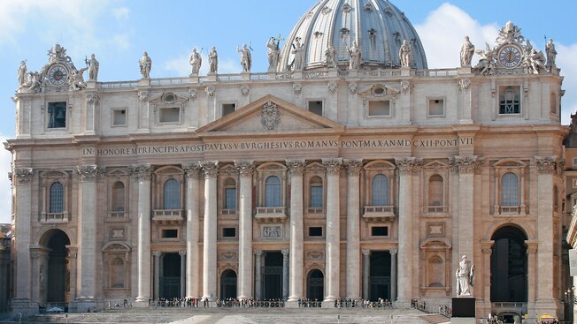 The exterior façade of a Roman-era building with giant columns and statues embellishing the roofline