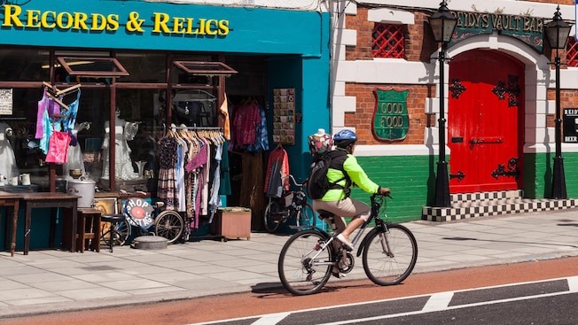 Um ciclista com capacete desce uma rua perto de uma loja com um sinal que diz Records and Relics Um ciclista com capacete desce uma rua perto de uma loja com um sinal que diz Records and Relics