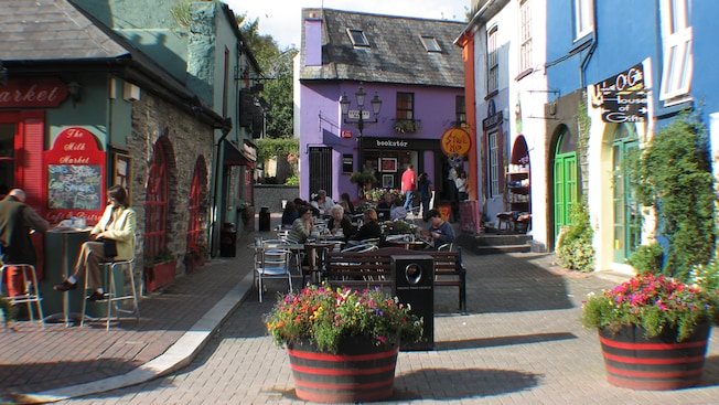 Quaint buildings line an outdoor patio and guests sit at tables eating Quaint buildings line an outdoor patio and guests sit at tables eating