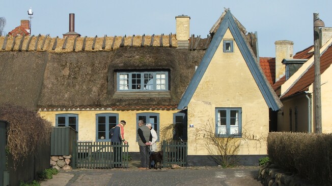 3 people standing in front of a stucco home with a thatched roof