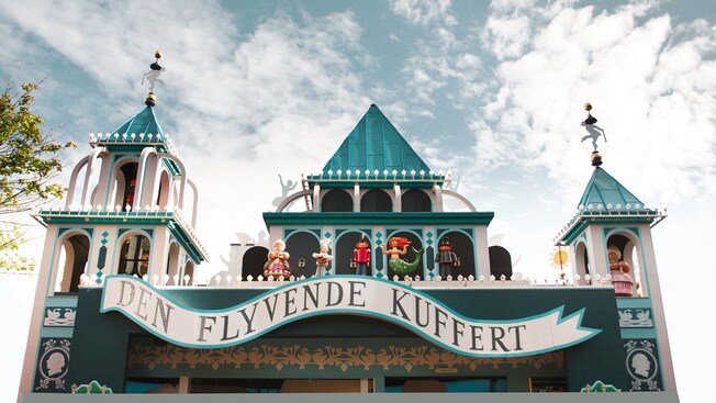A sign in Danish reads The Fly Trunk and hangs on a vintage style structure adorned with fairy tale figures