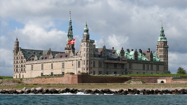 O Castelo de Kronborg voltado para o oceano com uma bandeira da Dinamarca tremulando à frente O Castelo de Kronborg voltado para o oceano com uma bandeira da Dinamarca tremulando à frente